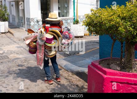 Unrecognizable Mexican vendor carrying traditional souvenirs on street in Chapala, Jalisco. Anonymous man loaded with colorful wicker hats, baskets Stock Photo