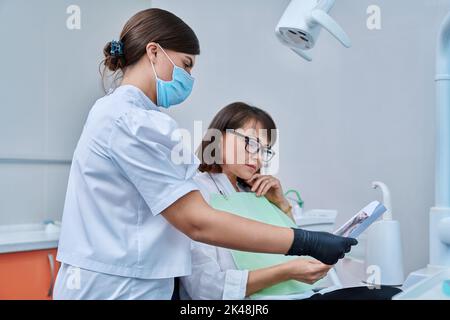 Female dentist talking to woman patient, discussing x-rays of teeth and jaws Stock Photo