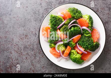 Natural mix salad of boiled broccoli, salted salmon and fresh red onion close-up in a plate on the table. horizontal top view from above Stock Photo