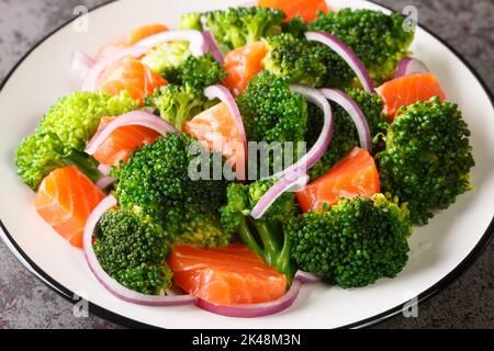Fresh healthy salad of boiled broccoli, smoked salmon and red onion close-up in a plate on the table. horizontal Stock Photo