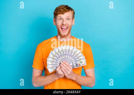 Photo of impressed ginger hair guy hold money yell wear orange t-shirt isolated on teal color background Stock Photo