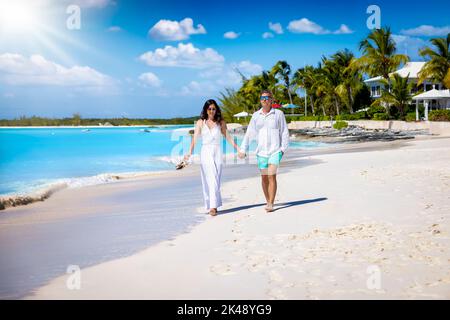 A beautiful couple in summer clothes walks hand in hand on a tropical beach Stock Photo