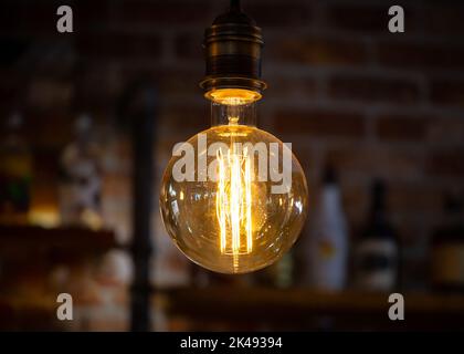 Light bulb with low energy filament illuminated lit up in dark room creating glowing light. Stock Photo
