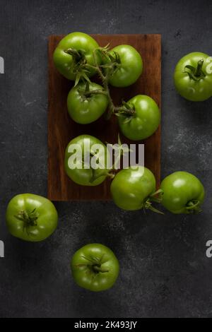 scattered tomatoes, freshly harvested green berries on a textured black table top surface, taken from above Stock Photo