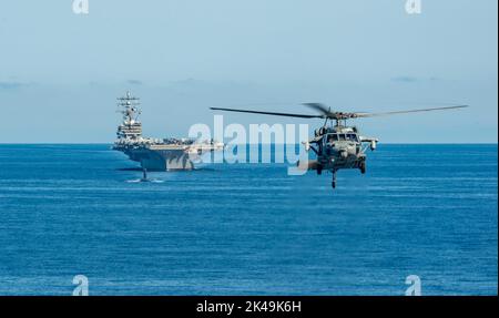 Busan, South Korea. 30th Sep, 2022. A U.S. Navy MH-60S Sea Hawk attached to the Golden Falcons of Helicopter Sea Combat Squadron 12, flys in front of a formation with the Nimitz-class, nuclear-powered super-carrier, USS Ronald Reagan and a Los Angeles-class fast-attack submarine with Submarine Group Seven during joint training operations with the South Korean Navy in the East Sea, September 30, 2022 near Busan, South Korea. Credit: MC3 Gray Gibson/US Navy Photo/Alamy Live News Stock Photo