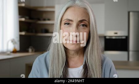 Portrait calm confident adult middle-aged woman pensioner granny mistress homeowner tender mature old lady with long grey hair posing in kitchen room Stock Photo