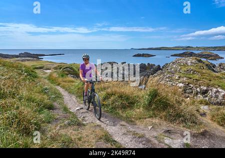 nice senior woman on mountain bike, cycling on the cliffs of Toormore,County Cork in southwestern Ireland Stock Photo