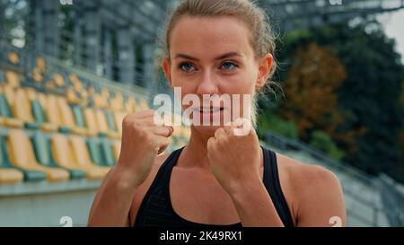 Motivated female fighter athlete with clenched fists standing in boxing stance punching air dynamic arms blows training endurance for competition Stock Photo