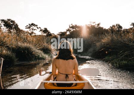 calm relaxed young woman sitting inside a kayak dressed in a swimsuit and holding the paddle against the light sailing on the lake near the forest Stock Photo