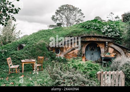 exterior of small wooden house with table chairs and chessboard with door and round windows buried in the mountain land hidden among greenery under Stock Photo
