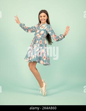 Full length cheerful teenager kid jump enjoy rejoice win isolated on blue background. Small child girl in summer dress jumping. Stock Photo