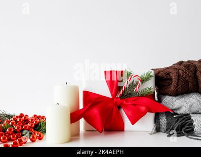 Christmas textile. Winter hygge. Festive home decor. Holiday discount. Gift box with red ribbon bow warm knitted sweater plaid candle set isolated on Stock Photo