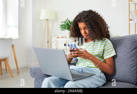 African American teenage girl who is addicted to her smartphone, laptop and social media. Stock Photo