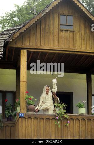 Nucsoara, Arges County, Romania, approx. 2000. Elderly woman on the porch of a wooden house wearing a traditional hand-made folk costume, spinning wool using the old fashioned way. Stock Photo