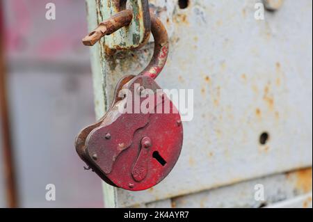An old red metal open lock hangs on the handle of an iron grey door Stock Photo