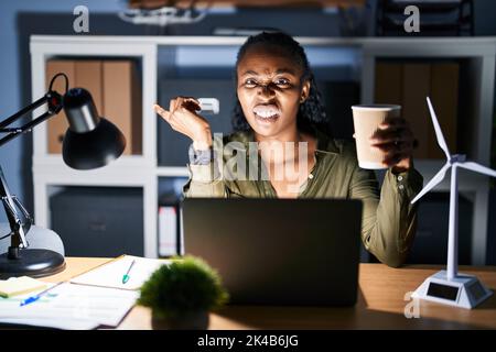 African woman working using computer laptop at night pointing aside worried and nervous with forefinger, concerned and surprised expression Stock Photo