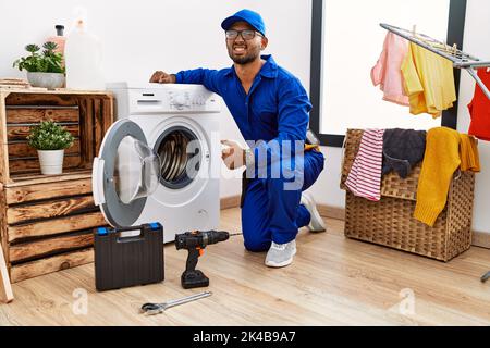 Young indian technician working on washing machine angry and mad screaming frustrated and furious, shouting with anger. rage and aggressive concept. Stock Photo