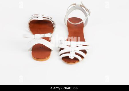 White leather women's sandals with low heels. It is located on a white surface. Close-up. Stock Photo