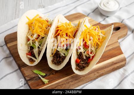 Homemade American Beef Tacos with lettuce, tomato and cheese on a wooden board, side view. Stock Photo