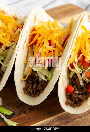 Homemade American Beef Tacos with lettuce, tomato and cheese on a wooden board, low angle view. Stock Photo