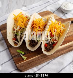 Homemade American Beef Tacos with lettuce, tomato and cheese on a wooden board, side view. Stock Photo