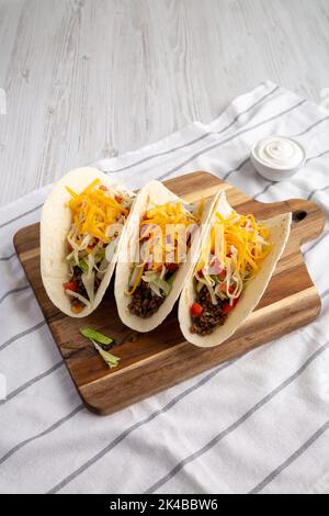 Homemade American Beef Tacos with lettuce, tomato and cheese on a wooden board, side view. Stock Photo