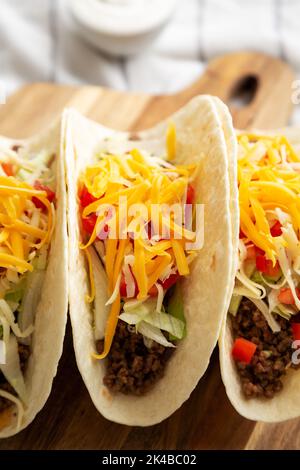 Homemade American Beef Tacos with lettuce, tomato and cheese on a wooden board, side view. Stock Photo