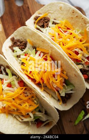 Homemade American Beef Tacos with lettuce, tomato and cheese on a wooden board, top view. Stock Photo