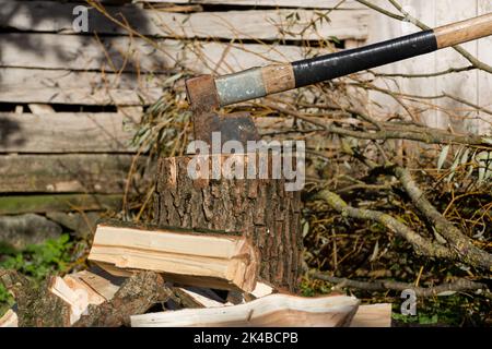 An old retro ax was stuck in a tree stump and cut wood around it on a sunny autumn day in the village. Close up, selective focus Stock Photo