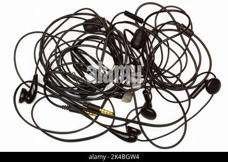 Old tangled headphones on a white background. Isolated. Black dusty dirty wired headphones with tangled wires. Audio Speakers, microphones, plugs Stock Photo