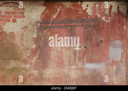 Old weathered painted wall background texture. Red dirty peeled plaster wall with falling off flakes of paint Stock Photo