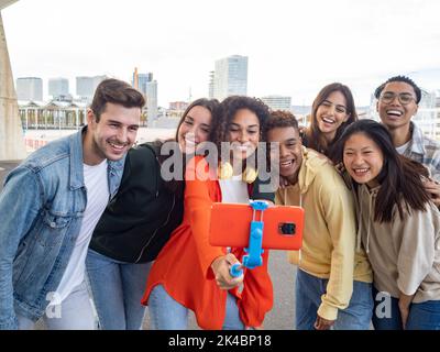 Group of diverse millennials recording a video or taking a photo for social media. Young people having fun with new technology  Stock Photo
