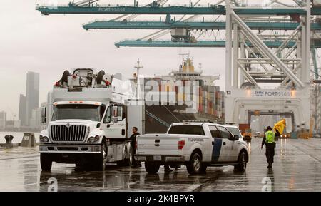 A U.S. Customs and Border Protection officer, right, shakes off his rain coat as he and a fellow officer wrap up scanning of shipping containers as they inspect incoming cargo at the Port of Miami in Miami Fla., Dec. 07, 2015. CBP Photo by Glenn Fawcett Stock Photo