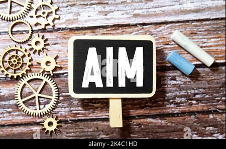 The word Aim on a strip of white paper. A red dart will be stuck in the word. Blue background Stock Photo