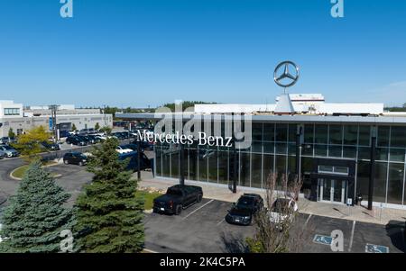 An aerial view out front of a modern Mercedes-Benz dealership, the famous Mercedes star emblem shining in the sun on a blue sky day. Stock Photo