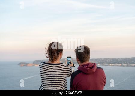 A couple sitting and taking selfies with the beautiful seascape at sunset Stock Photo