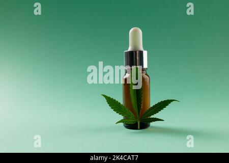 Image of bottle of cbd oil and marihuana leaf on green surface Stock Photo