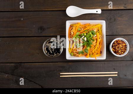 Overhead view of asian wok stir fry noodles with spoon and condiments on wood Stock Photo