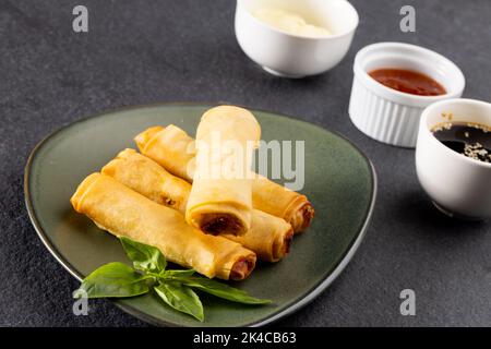 Overhead view of asian spring rolls on grey plate and condiments on grey background Stock Photo