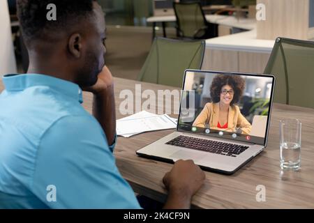African american businessman discussing with female coworker on videocall over laptop at office Stock Photo