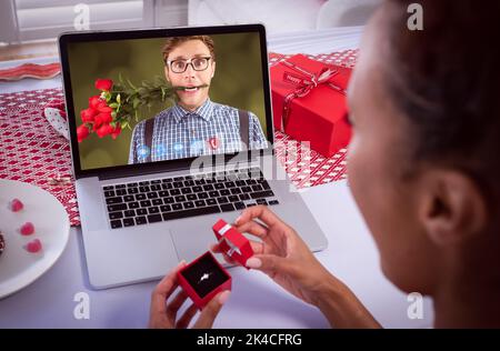 Diverse couple making valentines date video call man on screen with flowers between teeth and woman holding ring. online valentines day during quarant Stock Photo