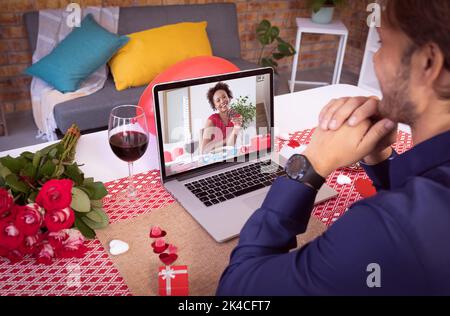 Diverse couple making valentines date video call the woman on laptop screen smiling. online valentines day during quarantine lockdown. Stock Photo