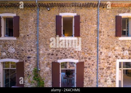 The stone facade of a large house with six open windows on two floors, two gutters on the sides Stock Photo