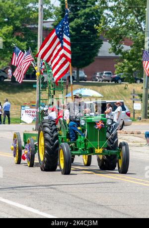 Eau Claire MI USA, July 4 2022; Farmer on an antique John Deere tractor, waves as he drives his classic vehicle in a 4th of July parade Stock Photo