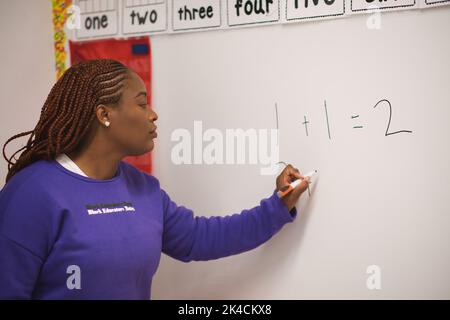 A confident African American female math teacher writing numbers on the whiteboard in the classroom Stock Photo