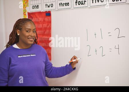 A confident African American female math teacher writing number on the whiteboard in the classroom Stock Photo