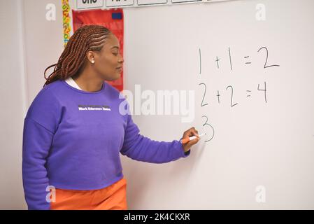 A confident African American female math teacher writing  numbers on the whiteboard in the classroom Stock Photo