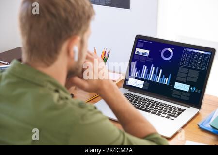 Caucasian businessman sitting at desk using laptop with graph and statistical data on screen. business communication and digital interface technology Stock Photo