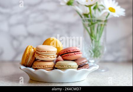 Simple and elegant still life of sweet french macarons on a white plate with white daisies in the background Stock Photo