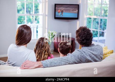 Family watching television while sitting on sofa at home Stock Photo